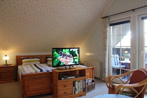 Ett sovrum med en säng, en tv på ett träställ, ett nattduksbord, en stol och ett fönster med gardiner.
