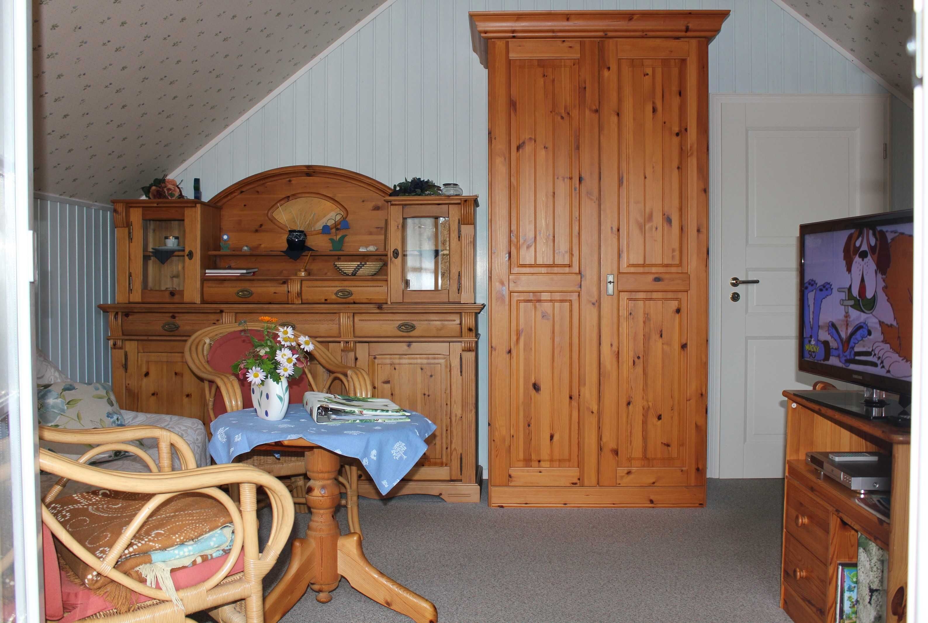 Ein Zimmer mit einem Holzkasten, einem Fernseher und einem Korbstuhl.