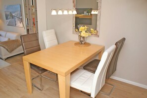 Un coin repas avec une table en bois, des chaises blanches et marron, un vase avec des fleurs jaunes et un miroir surmonté de lampes.
