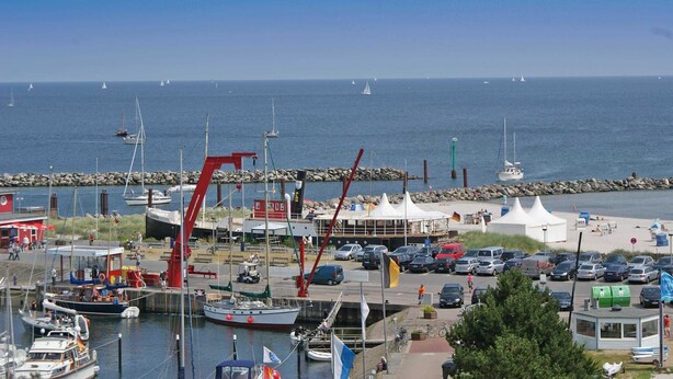 A marina with boats, a red crane, and a beach area with tents and cars.