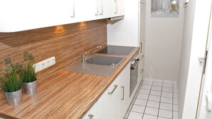 A modern kitchen with a wooden countertop, stainless steel sink, and white cabinets. There are two small potted plants on the counter.