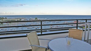 A balcony with a view of the sea and marina. There are wicker chairs and a table with a glass.