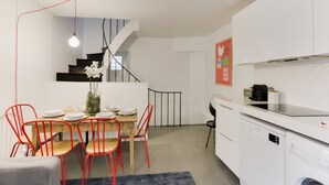 Een moderne keuken met witte kastjes, een houten eettafel, rode stoelen en een trap naar een zolderruimte.