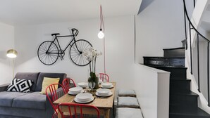 Een moderne woonkamer met een eettafel voor vier personen, een grijze bank, rode stoelen en een fiets aan de muur.