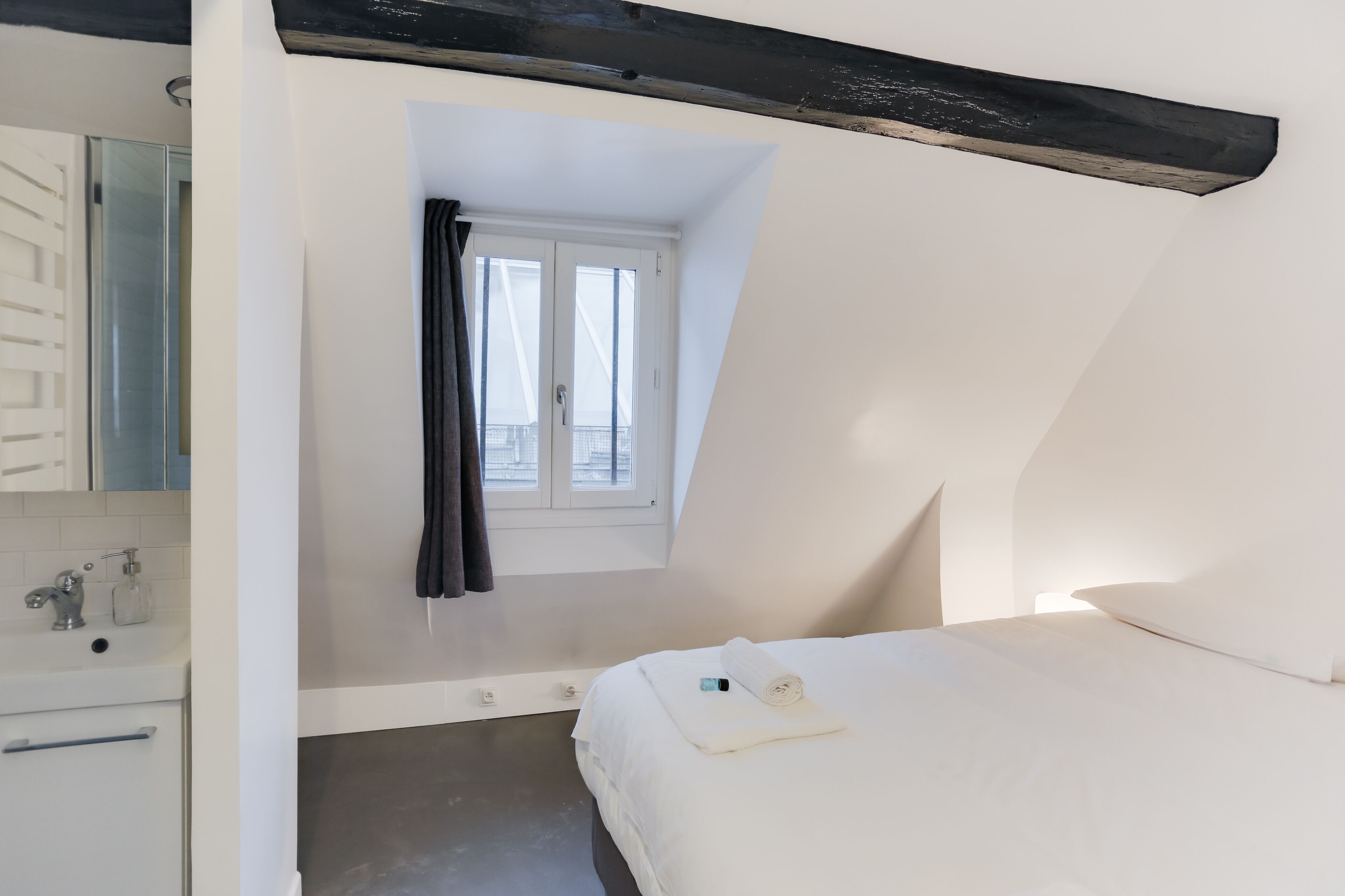 A bedroom with a bed, a window, a bathroom with a mirror, and a towel on the bed.