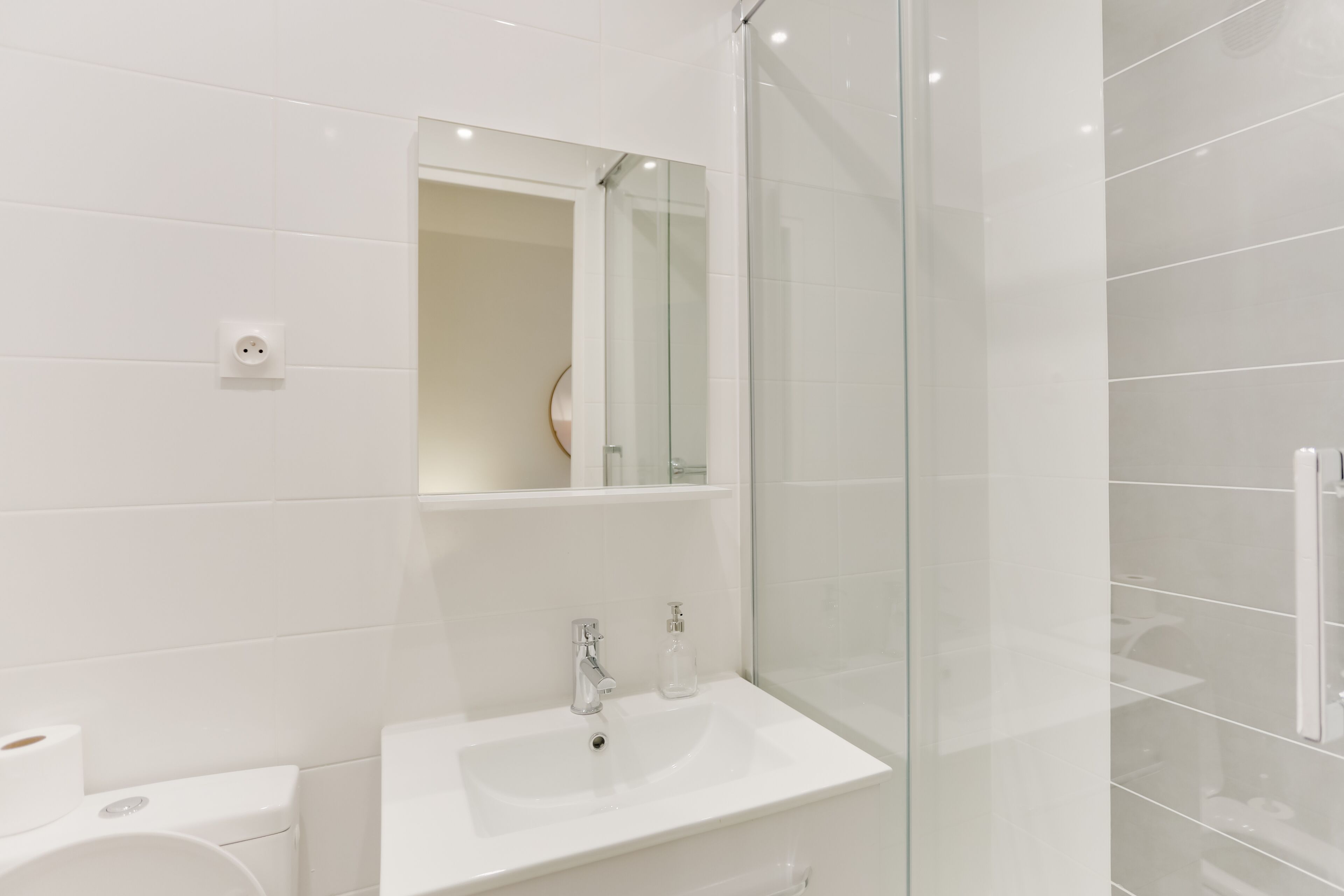Un baño moderno con lavamanos blanco, espejo y cabina de ducha de vidrio.