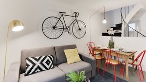 Een moderne woonruimte met een grijze bank, een eettafel met rode stoelen, en een zwarte fiets aan de muur.