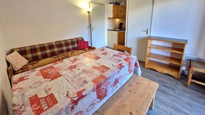 Una habitación acogedora con una cama, un banco, una mesa de madera y una kitchenette al fondo.