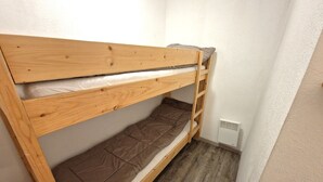 Una cama individual en literas en una habitación pequeña con una pared blanca y un respiradero en el suelo.