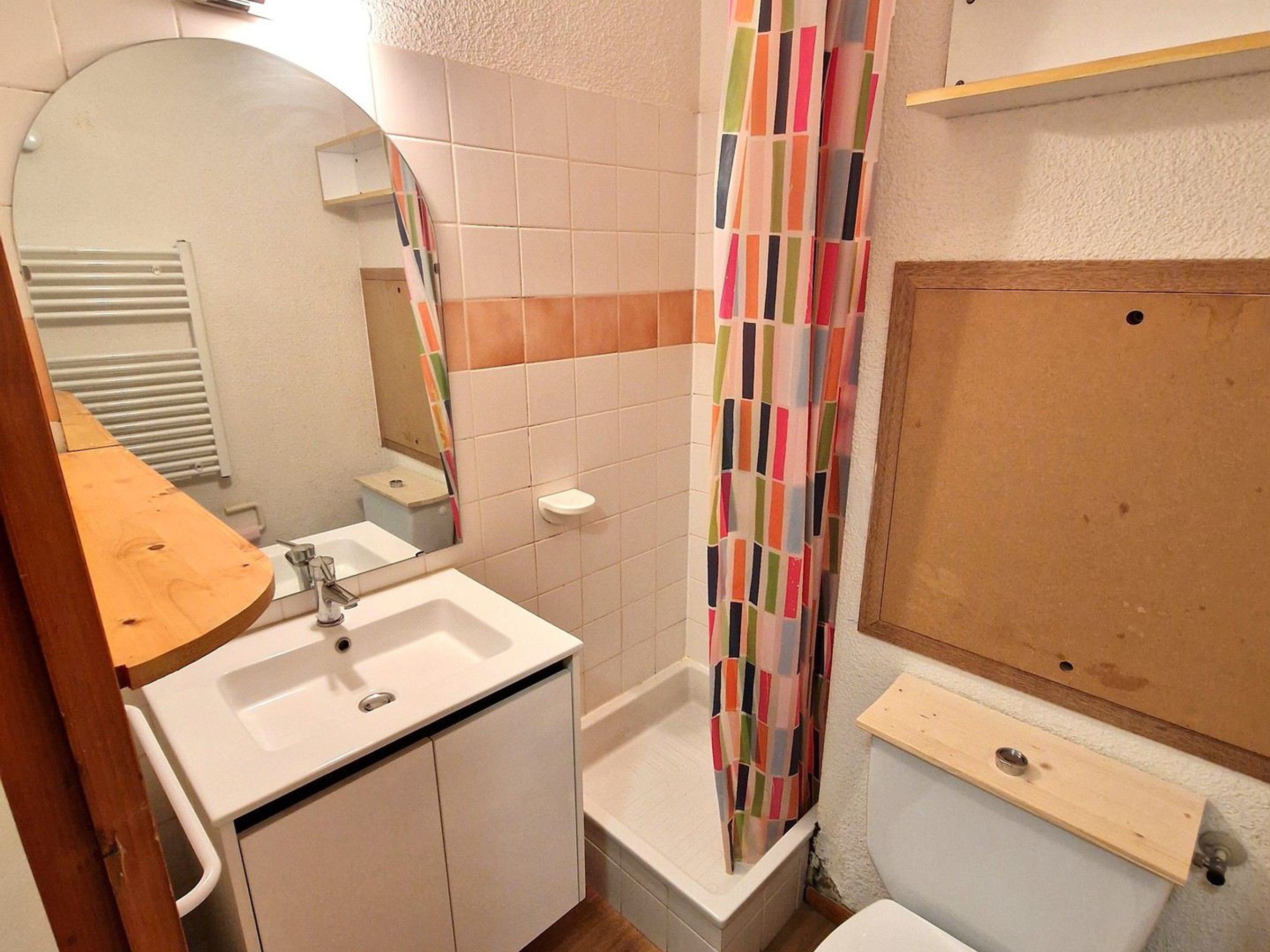 Ein Badezimmer mit einem weißen Waschbecken, Spiegel und einer Dusche mit einem bunten, gestreiften Vorhang.