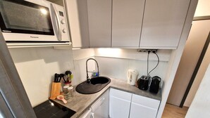 A compact kitchen with a microwave, sink, and a small countertop with a toaster and a kettle. - 2-Room + Cabin Apartment for 4-6 in Heart of Station - WiFi & Balcony (Valfréjus)