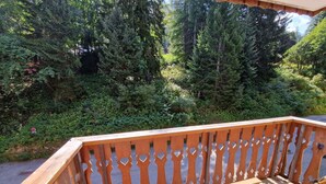 A wooden deck with a railing, benches, and a view of a forested area. - 2-Room + Cabin Apartment for 4-6 in Heart of Station - WiFi & Balcony (Valfréjus)