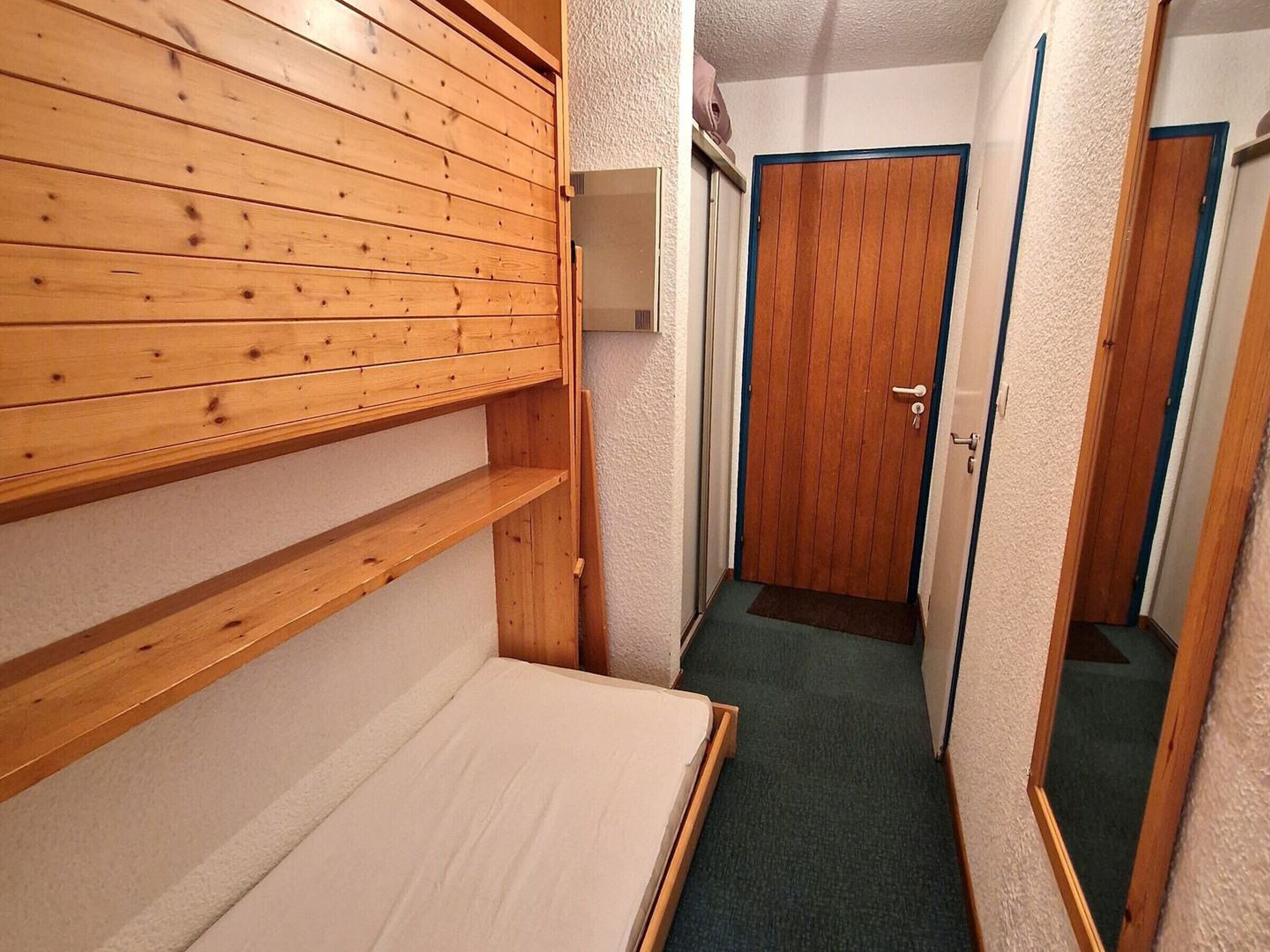 A narrow hallway with a wooden shelf, a door, and a mirror.