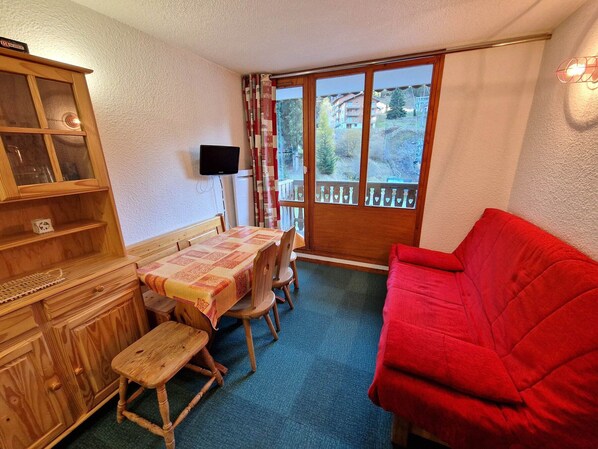 Une pièce chaleureuse avec une table à manger en bois, des chaises, un canapé rouge et un buffet en bois.