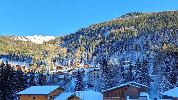 Un albergue de montaña con varias construcciones de madera, rodeado de árboles nevados y un cielo azul despejado.