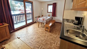 Una cocina compacta con mesa de comedor, estufa y un ventanal con cortinas.