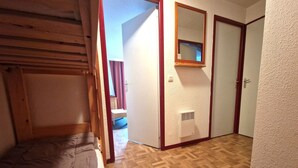 Una habitación con una cama litera, una puerta de madera, un espejo y un respiradero blanco en la pared.