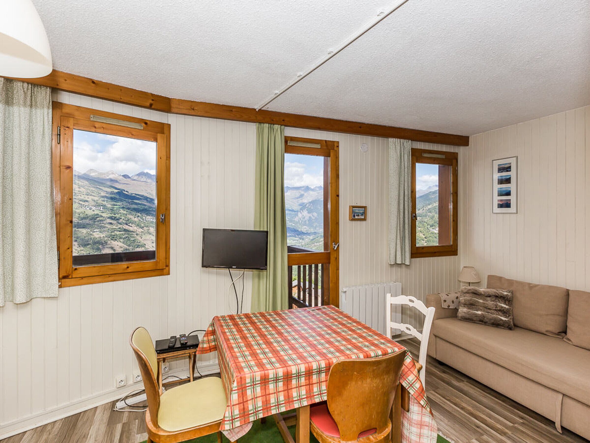 Une pièce comprenant une table et des chaises, un canapé, un téléviseur et des fenêtres donnant sur la montagne.