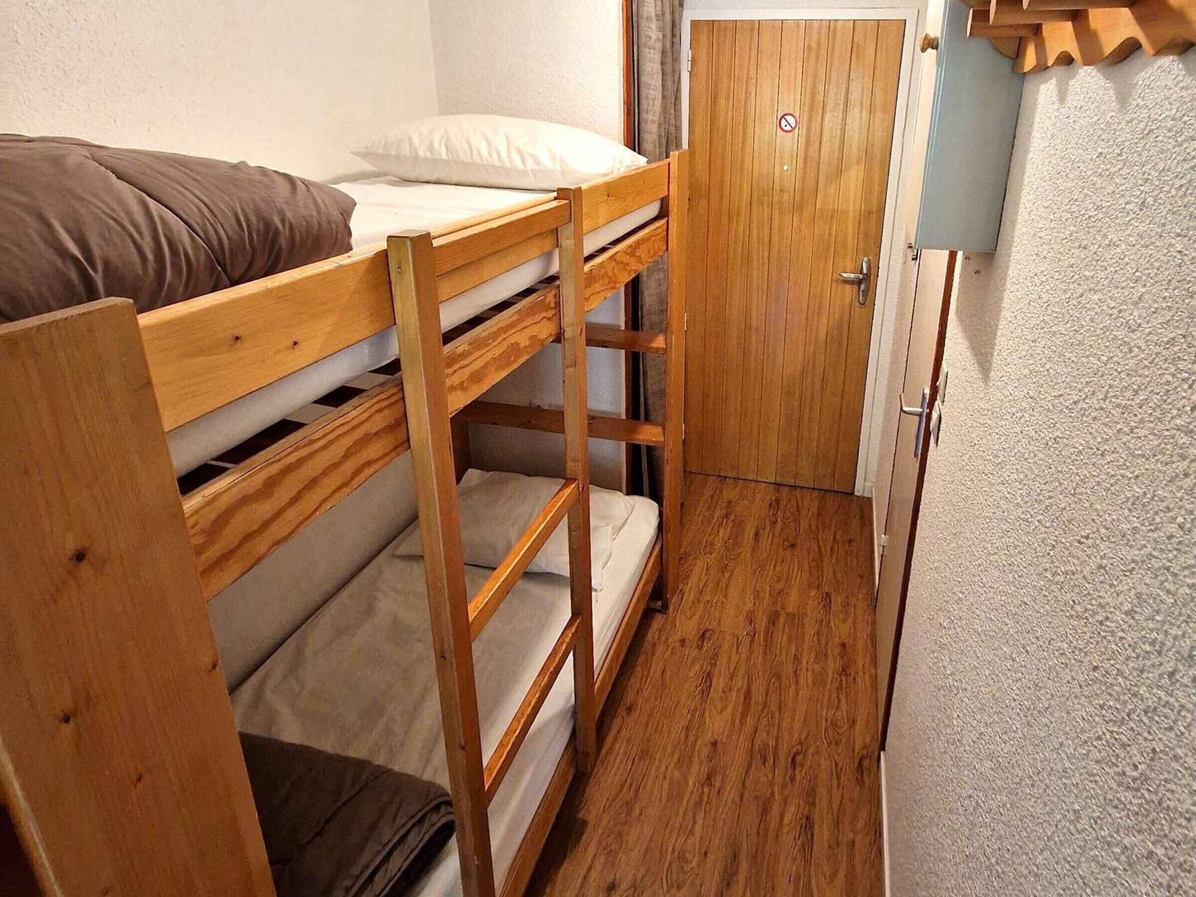 Une chambre avec un lit superposé, une porte en bois et un petit placard.