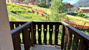 A wooden balcony with a view of a mountainous area, including houses and a railway track. - Renovated studio for 2-3 in Valfréjus, balcony and slope view (Valfréjus)