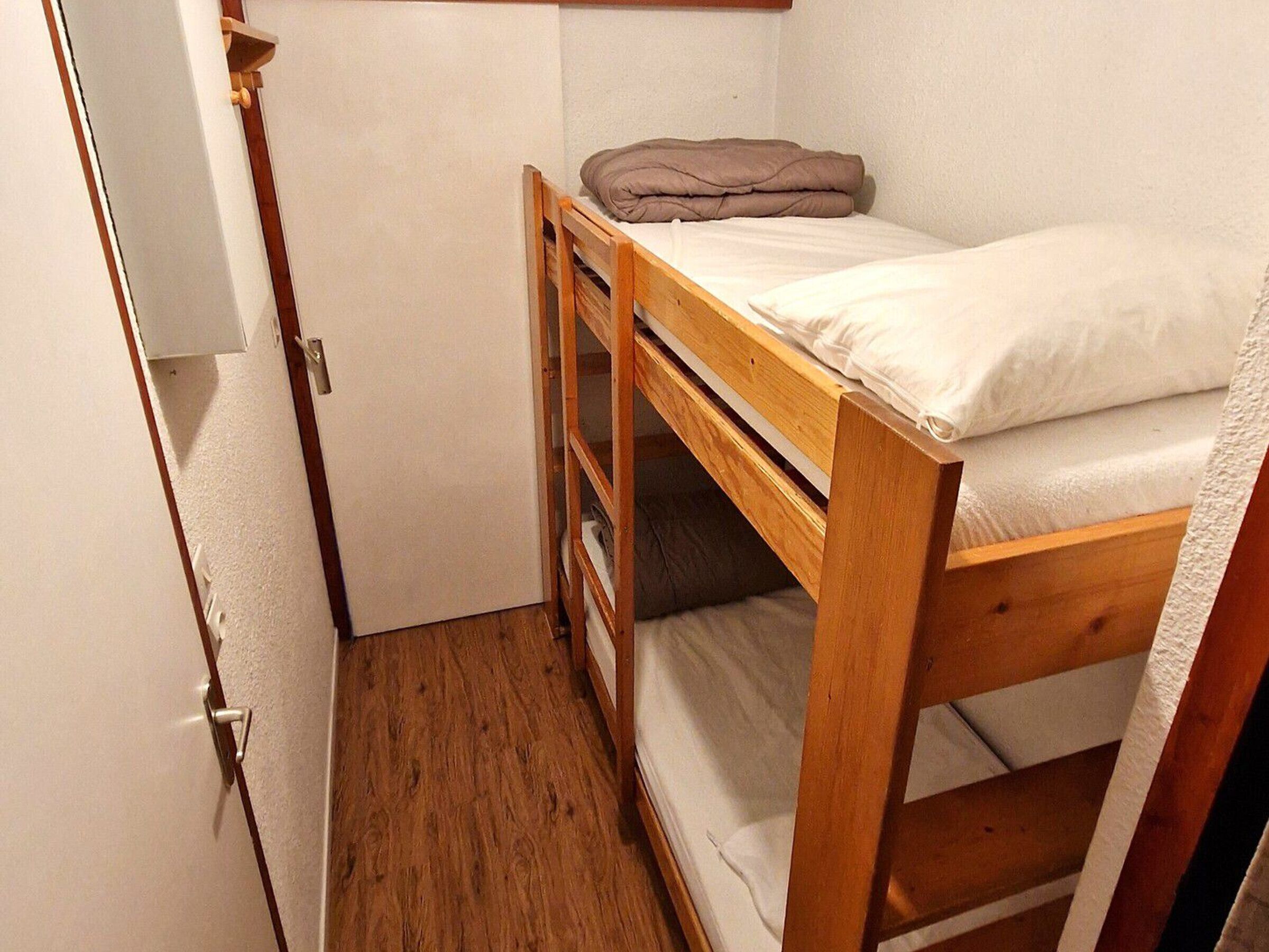 A small, compact room with a bunk bed, a wooden wardrobe, and a white door.