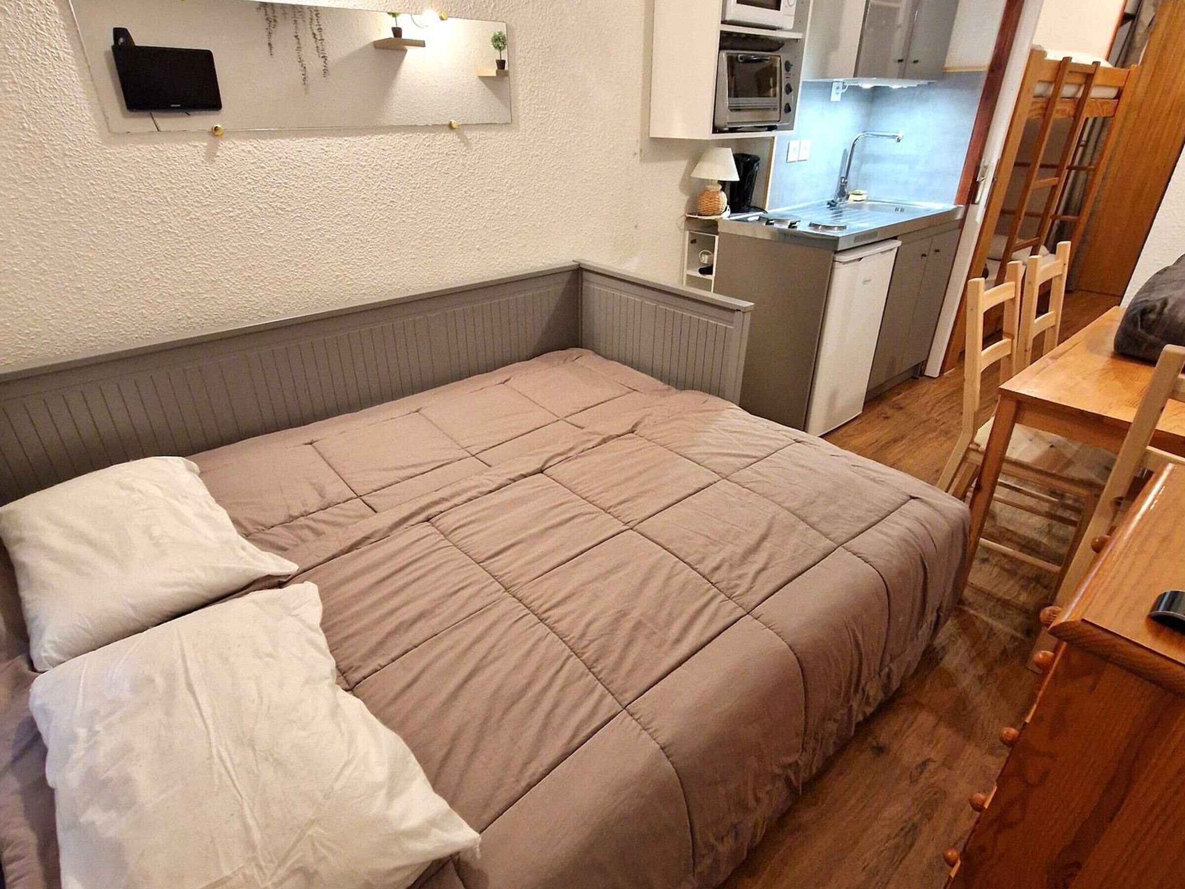 Une chambre à coucher avec un lit, une table de chevet, une chaise et, au fond, un coin cuisine.
