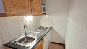 A compact kitchen with a sink, stove, and wooden cabinets. - Valfréjus: 2-room + cabin, central location, 4/6 people (Valfréjus)