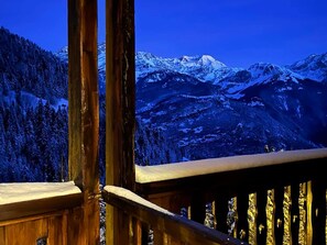 Een houten balkon met uitzicht op besneeuwde bergen en een bebost gebied.
