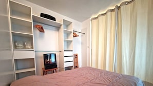 A bedroom with a bed, a TV on a wooden stand, built-in shelving, and a window with curtains. - Cozy 2-Room Apartment for 4/6 People, 32m² - Ski-in/Ski-out, Close to Village Center (Valfréjus)