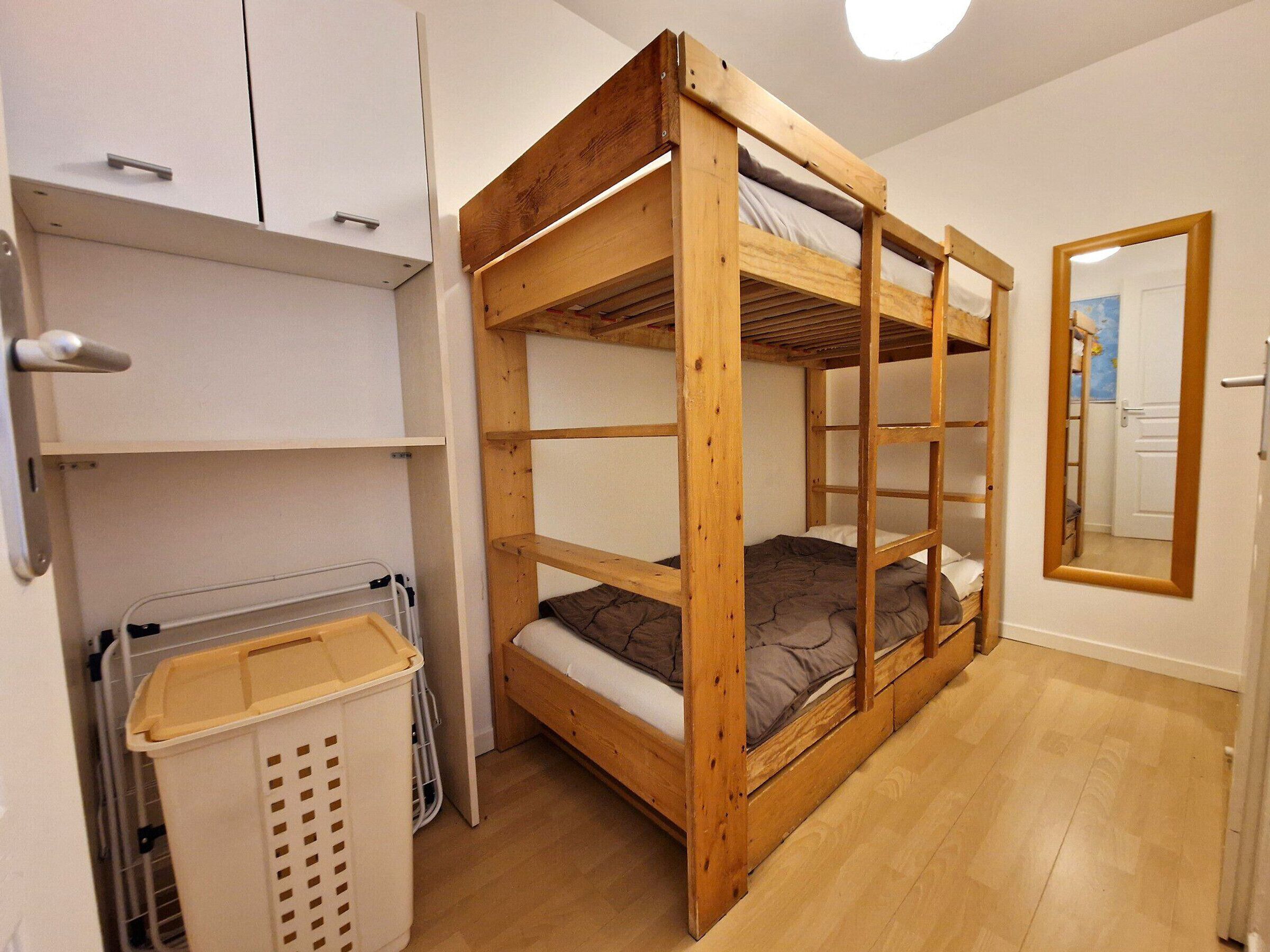 A bunk bed room with wooden frames, white walls, and a mirror on the wall.
