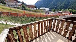 A wooden balcony with a view of a mountainous area, a wooden fence, and a paved walkway. - Cozy 2-Room Apartment for 4/6 People, 32m² - Ski-in/Ski-out, Close to Village Center (Valfréjus)