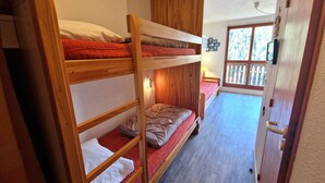 A dormitory room with bunk beds, a wooden door, and a window with a view of trees.