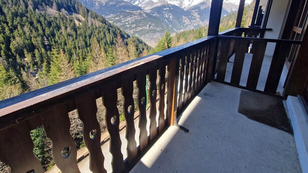 A balcony with a view of snow-capped mountains and dense forest.