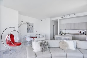 Una sala de estar moderna con un sofá blanco, un sillón rojo y una cocina con mesa y sillas.