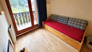 A room with a wooden bed, a sliding glass door to a balcony, and a wall-mounted light fixture. - Charming studio for 2-3 people with balcony in Valfréjus (Valfréjus)