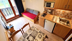 A compact kitchen with wooden cabinets, a microwave, a small sink, and a dining table with chairs. - Charming studio for 2-3 people with balcony in Valfréjus (Valfréjus)