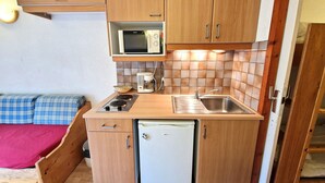 A compact kitchen with wooden cabinets, a microwave, a sink, a small refrigerator, and a stove. - Charming studio for 2-3 people with balcony in Valfréjus (Valfréjus)