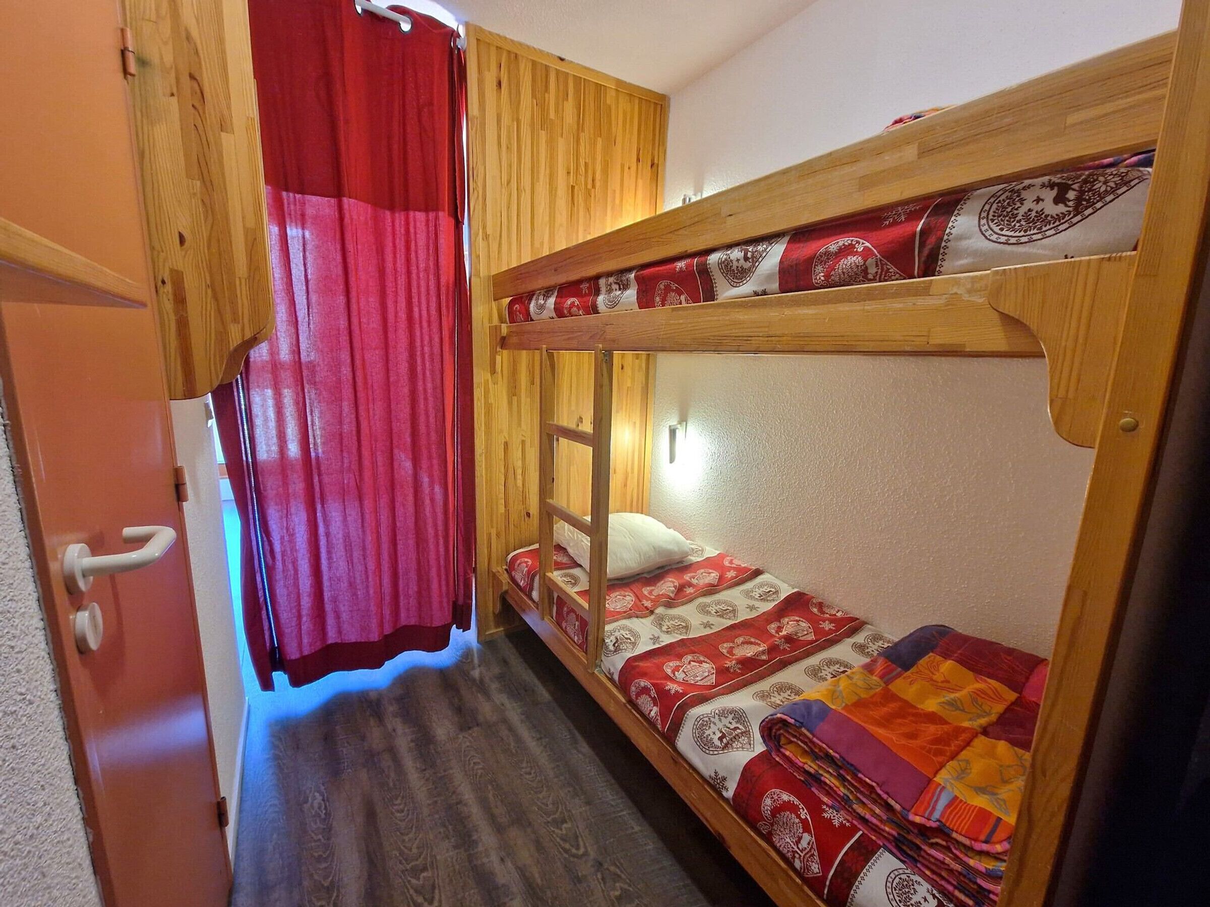 A bunk bed room with a wooden headboard, a red curtain, and a small window with a light fixture.