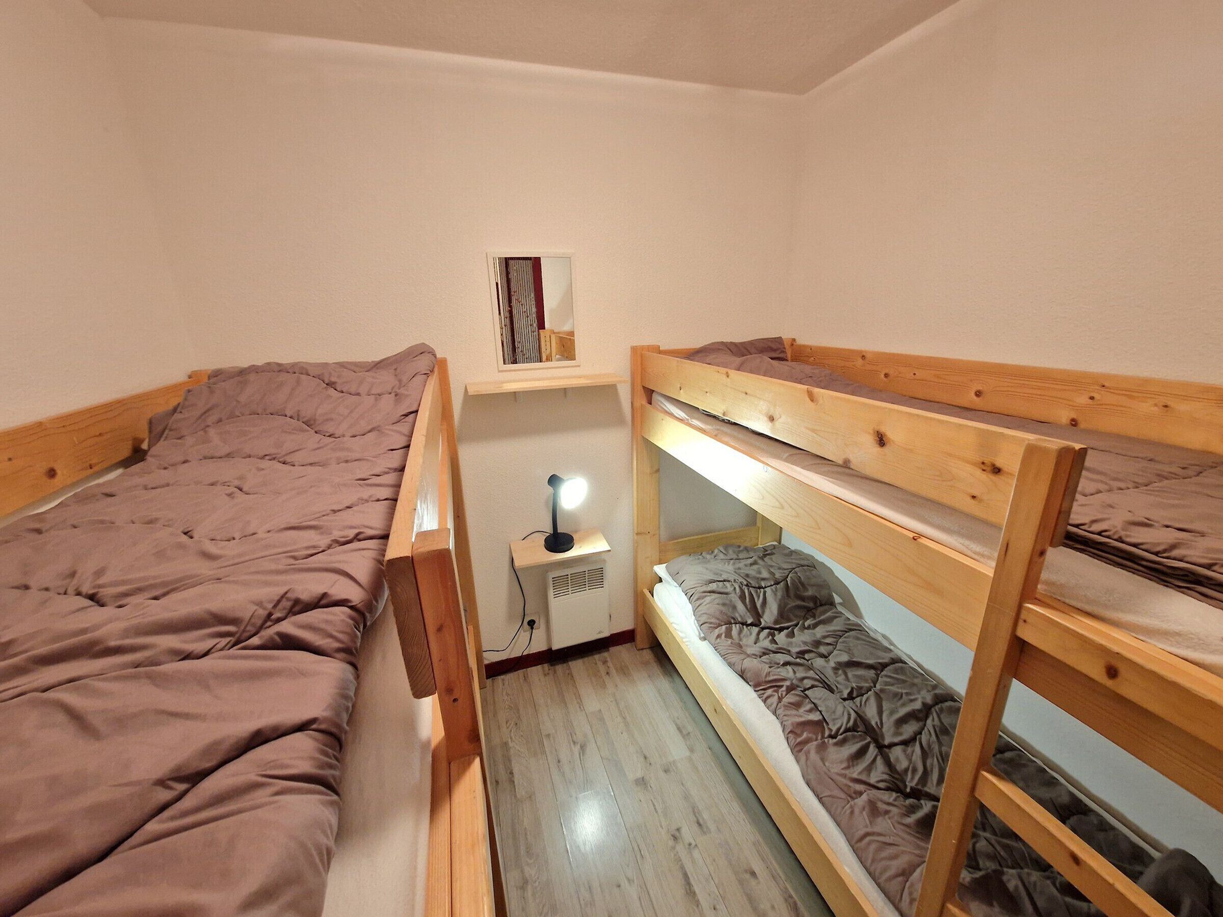 A dormitory room with two bunk beds, a small desk with a lamp, and a shelf with books.