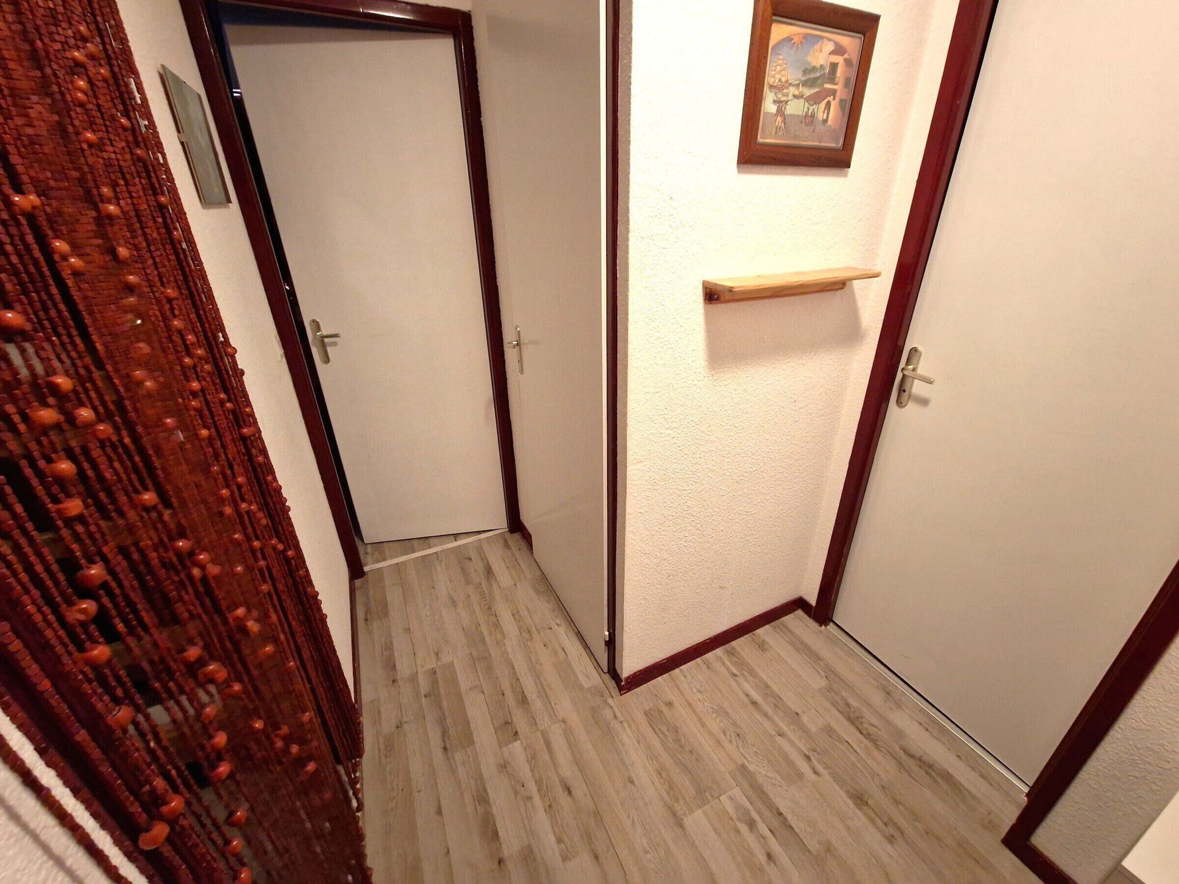 A hallway with a wooden door, a small wooden shelf, and a framed picture on the wall.