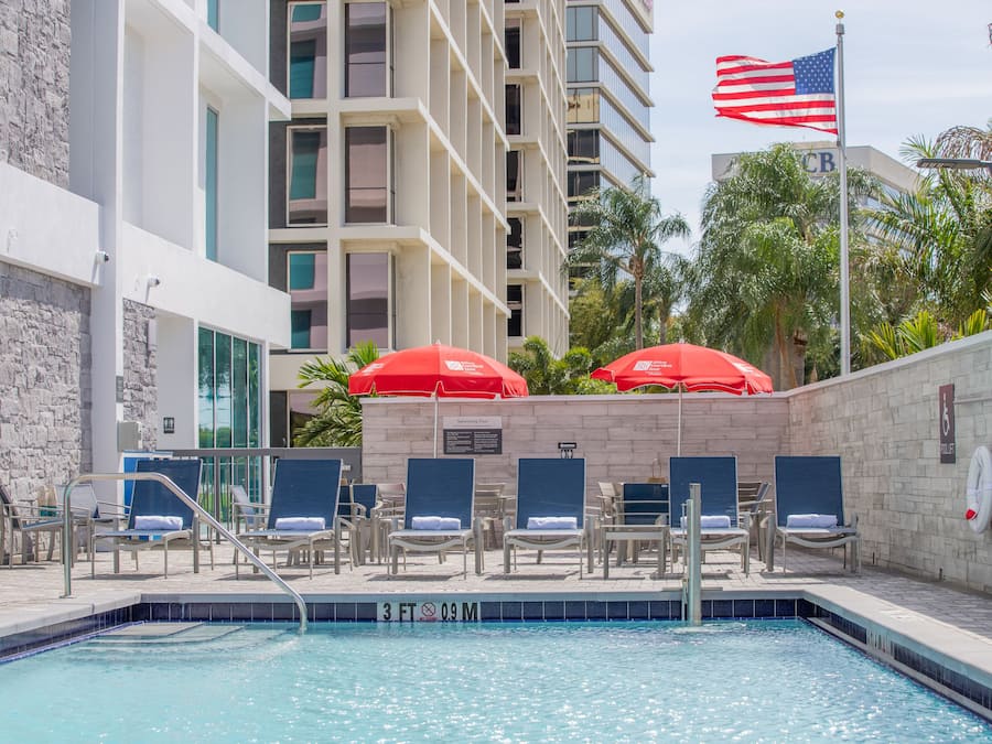 Piscina com espreguiçadeiras e guarda-sóis, um flutuador e uma bandeira americana.