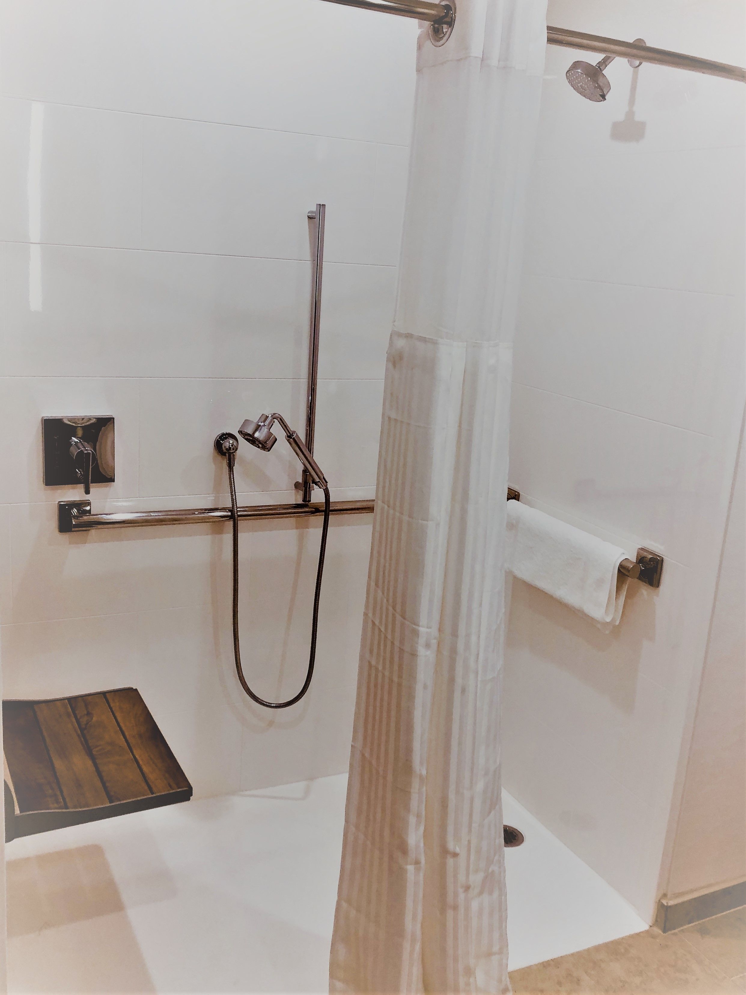 A modern bathroom with a shower, a towel rack, and a wooden shelf.