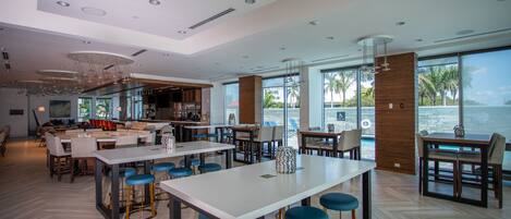 Un moderno vestíbulo de hotel con zona de bar, asientos y grandes ventanales con vistas al mar.
