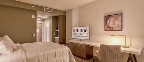 A hotel room with a bed, desk, chair, and a sign indicating it's a Hilton Garden Inn.