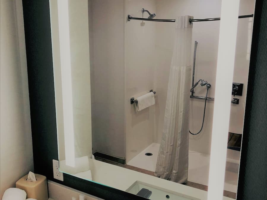 A modern bathroom with a large mirror, a shower with a glass door, and a sink with toiletries.