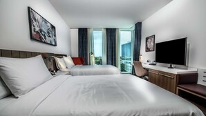A hotel room with two beds, a desk with a flat-screen TV, a chair, and a window with curtains. - Hilton Garden Inn West Palm Beach I95 Outlets (West Palm Beach)