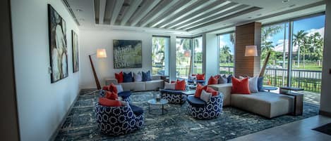A spacious living area with a large window, a ceiling with wooden slats, and a mix of seating options including bean bags and sofas.