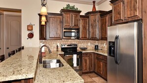 A kitchen with granite countertops, stainless steel appliances, wooden cabinets, and a hanging light fixture.