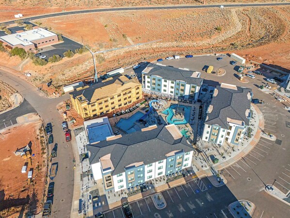 An aerial view of a hotel complex with multiple buildings, parking areas, and a swimming pool.