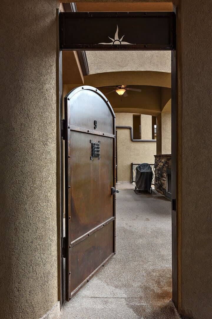 A metal door with a keypad lock, leading to a room with a stone fireplace and a covered grill.